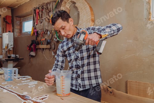 Preview: Carpenter mixing epoxy resin with an electric mixer in liquid cup in workshop
