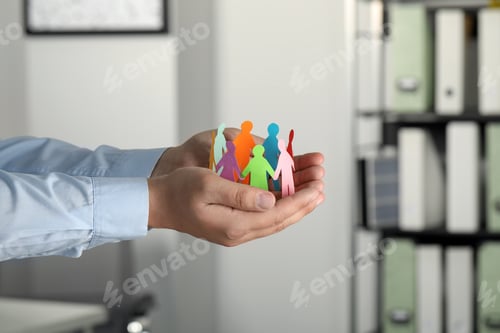Preview: Man holding paper human figures in office, closeup. Diversity and Inclusion concept