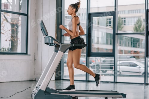 Preview: side view of african american sportswoman running on treadmill at gym