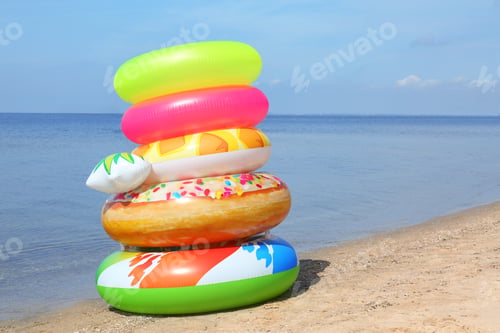 Preview: Stack of different bright inflatable rings on sandy beach near sea. Space for text