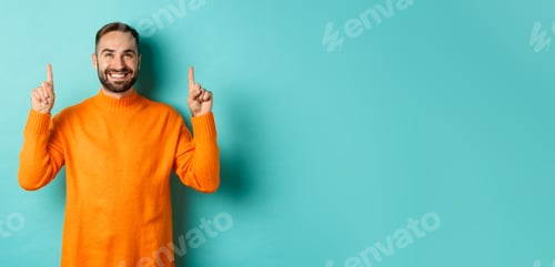 Preview: Satisfied and happy buyer pointing fingers up, smiling pleased, standing in orange sweater against