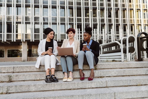 Preview: three multiracial businesswomen, on outdoor meeting video call, sitting on building stairs