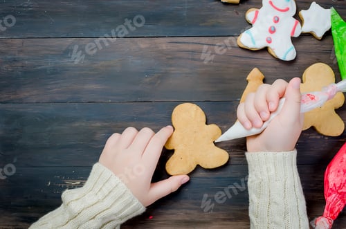 Preview: Happy little girl decorating a christmas gingerbread cookies using colored glazeon wooden table