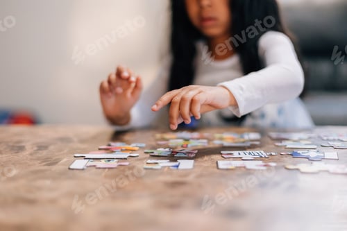 Preview: Diverse toddler girl at home with pretty black hair entertaining herself by solving simple puzzle