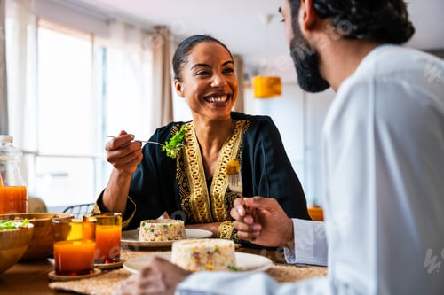 Preview: Happy beautiful young arab couple with emirati clothing having meal together at home