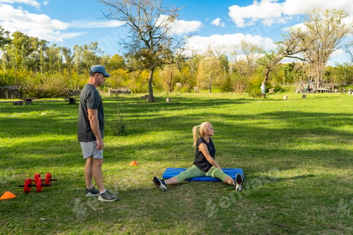 Preview: Woman doing stretching exercises with trainer outdoors