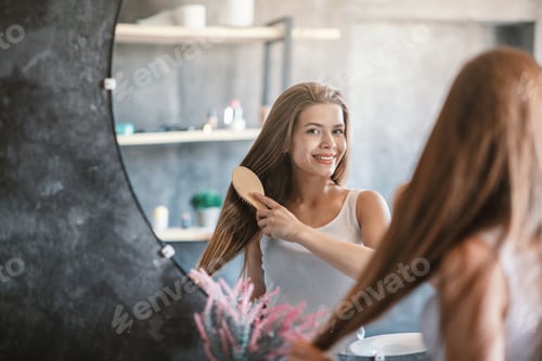Preview: Happy Woman Brushing Hair in Front of Mirror