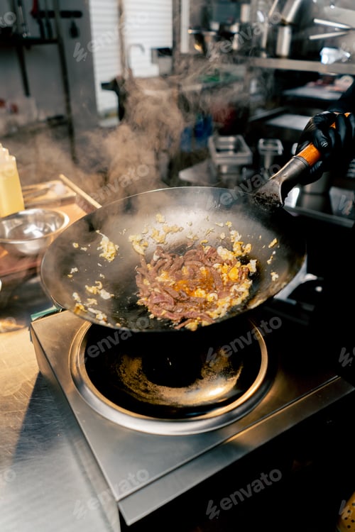 Preview: close-up of a frying pan with egg and meat over the stove with hand in a throw to mix the contents
