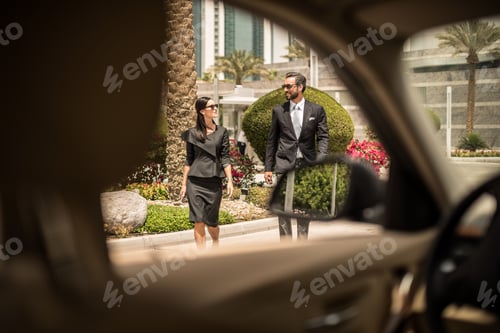 Preview: Car window view of businesswoman and man walking outside hotel, Dubai, United Arab Emirates