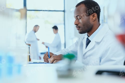 Preview: African american scientist in white coat taking notes while working in laboratory, laboratory