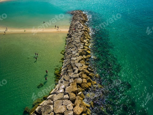 Preview: Aerial view of a rocky barrier in the crystal clear sea water with people resting