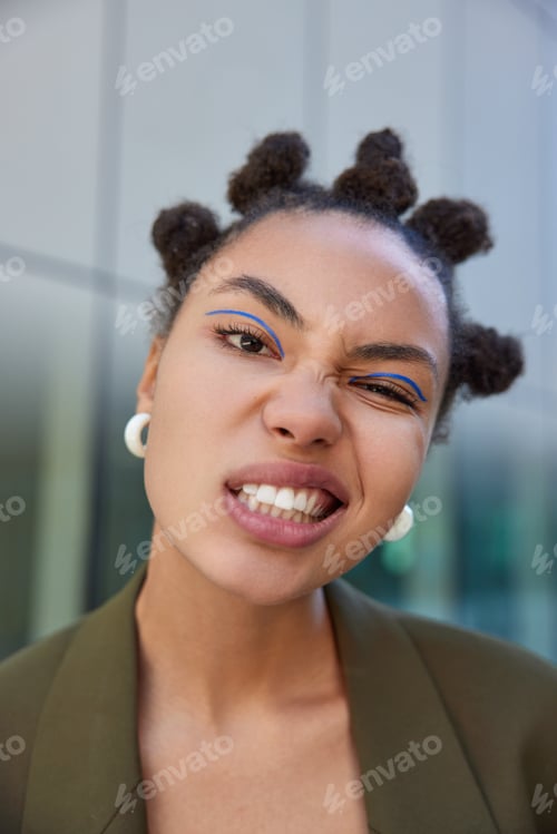 Vista previa: Close up shot of fashionable young woman with bun hairstyle has cheeky expression clenches teeth wea