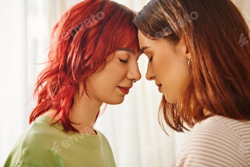 Preview: peaceful young lesbian couple with closed eyes standing next to each other at home, bliss and love