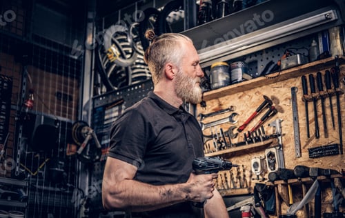 Preview: Elderly man craftsperson with drill around bench in workshop