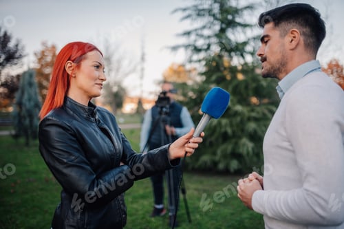 Preview: Journalist interviewing businessman in park with cameraman filming