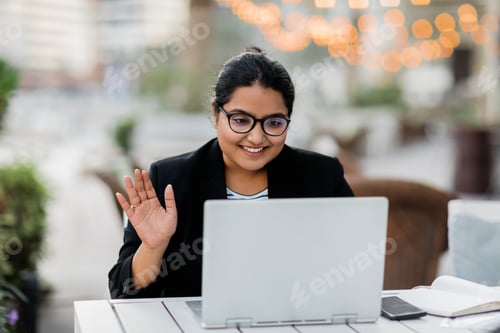 Preview: A young Indian woman is holding a video conference sitting in a cafe on the terrace. Freelance, onli