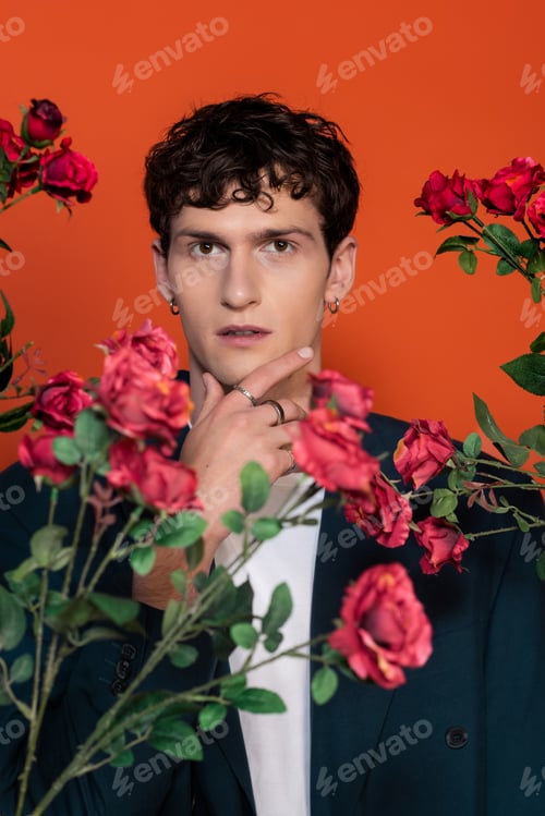 Preview: Portrait of stylish man touching chin near roses isolated on red