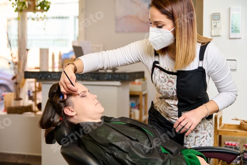 Preview: young hairdresser putting makeup on a woman in a beauty salon