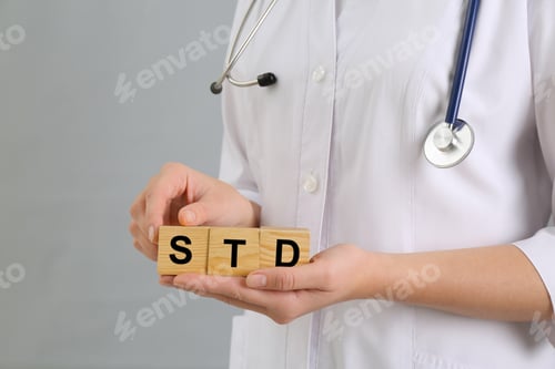 Preview: Doctor holding wooden cubes with abbreviation STD on grey background, closeup