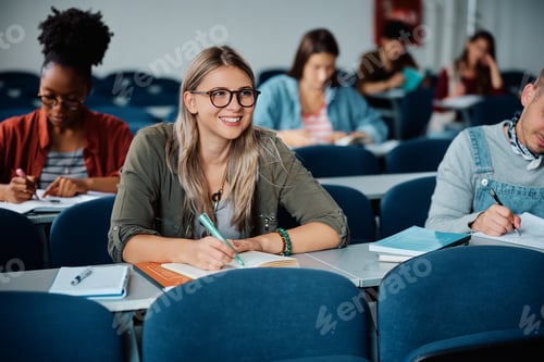 Preview: Happy female student taking notes while attending a lecture at the university.