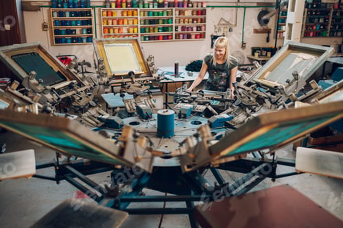 Preview: Female graphic worker operating screen carousel printing press at factory