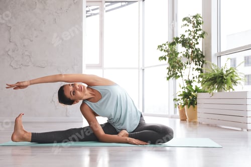 Preview: Young woman practicing revolved head to knee asana in yoga studio. Parivrtta Janu Sirsasana pose