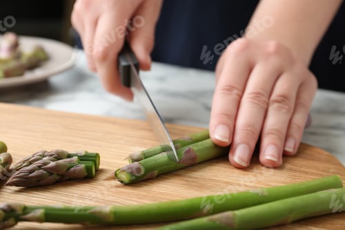 Preview: Woman cutting asparagus on wooden board, closeup