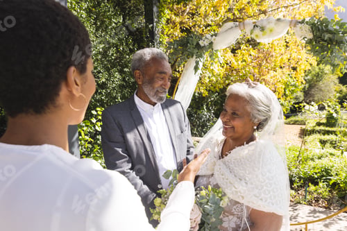 Preview: Biracial female marriage officiant and happy senior couple during wedding in sunny garden