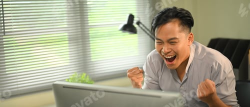 Preview: Excited young businessman celebrating success while working on computer