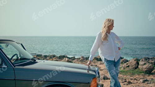 Preview: Stylish model posing retro car at summer seacoast. Woman standing sunny beach.