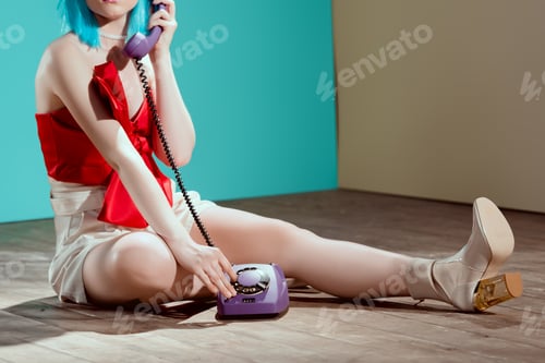 Preview: cropped shot of girl in blue wig talking by telephone while sitting on floor