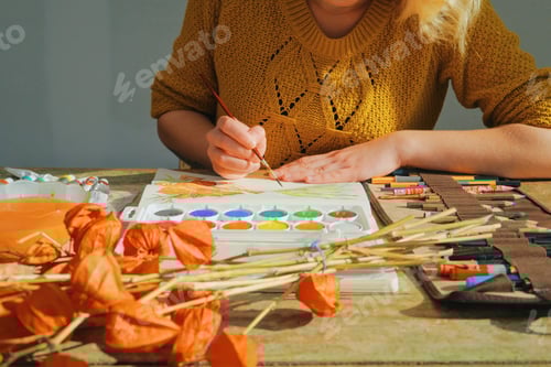 Preview: Female artist painting a picture of a flower with brush and watercolors - art is property released