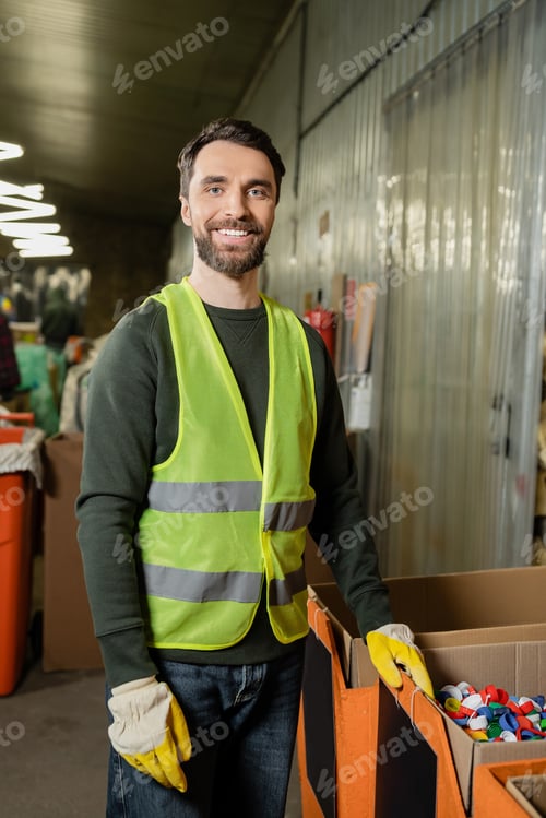 Preview: cheerful sorter in high visibility vest and protective gloves looking at camera while standing