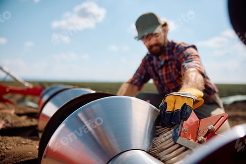 Preview: Close up of agronomist setting up disc harrows on a tractor while plowing the land.