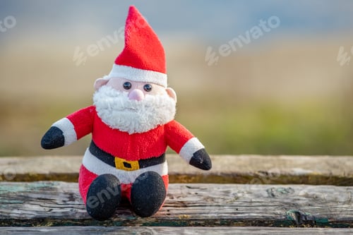 Preview: Close up of small santa clause toy on wooden bench outdoors.