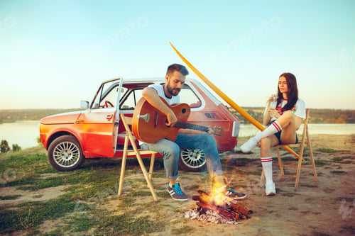 Preview: Couple sitting and resting on the beach playing guitar on a summer day near river