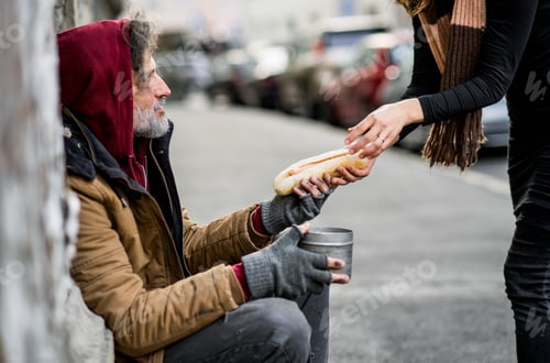 Preview: Unrecognizable woman giving food to homeless beggar man sitting in city.