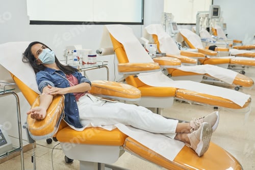 Preview: Woman in protective mask donating blood in modern clinic