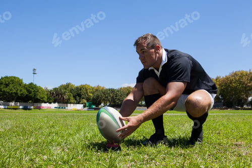 Preview: Rugby player holding ball while kneeling on grass