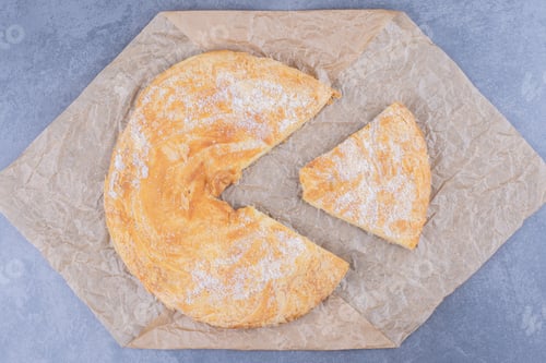 Preview: A round delicious pastry with sugar powder on a tablecloth
