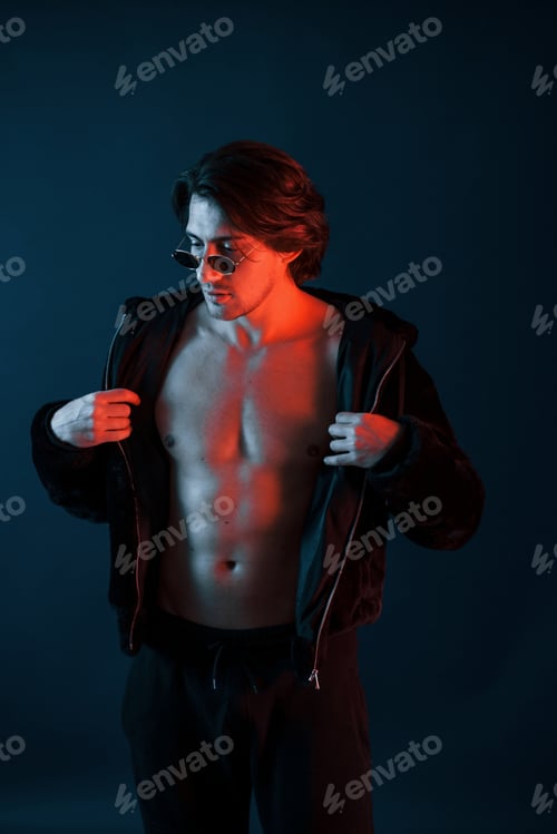 Preview: Beautiful man in glasses and black clothes is in the studio with blue neon lighting