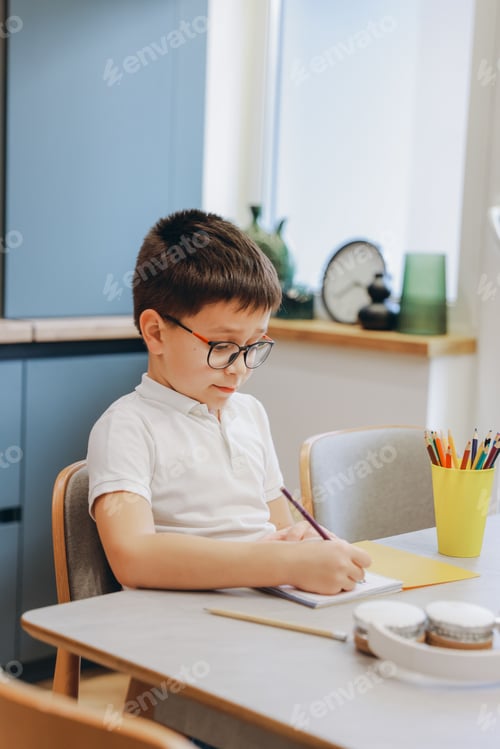 Preview: Young Student Wearing Glasses Doing Homework and Writing on Notebook at Home