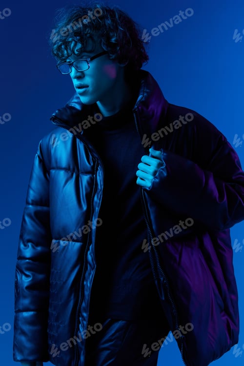 Preview: Man in winter down jacket model posing with glasses, hipster lifestyle, portrait blue background