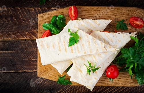 Preview: Grilled tortilla wraps with chicken and fresh vegetables on wooden board.