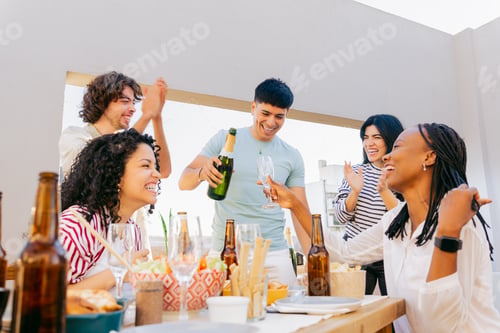 Preview: In front of a table on a terrace, Latin friends celebrate with champagne.