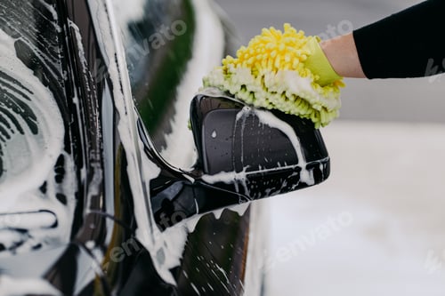 Preview: Mans hand holding sponge for washing car. Black auto with soap bubbles