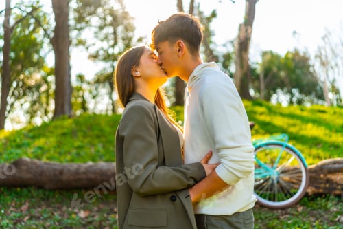 Preview: Young couple kissing in the park with bicycle in background at sunset