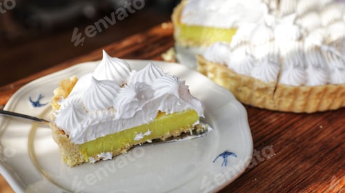Preview: Sliced delicious lemon tart topped with white whipped cream against a background of a wooden table