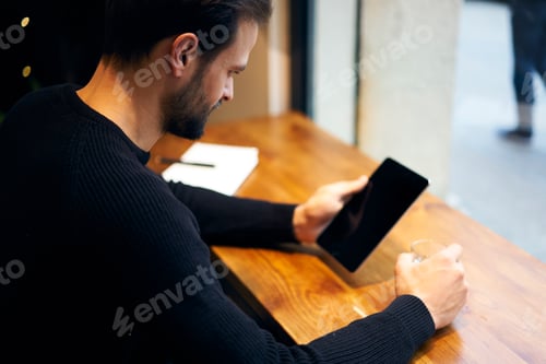 Preview: Focused ethnic man browsing tablet