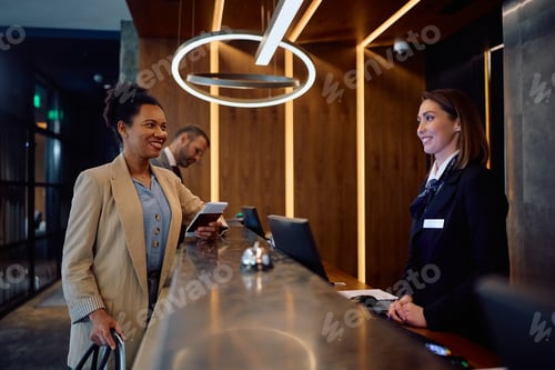 Preview: Happy black businesswoman checking in at hotel reception desk.